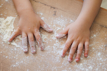 Children's hands in flour on a wooden surface during baking.