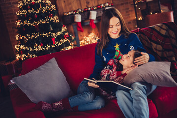 Portrait of two people mother daughter hold book cuddle speak sofa festive christmas time...