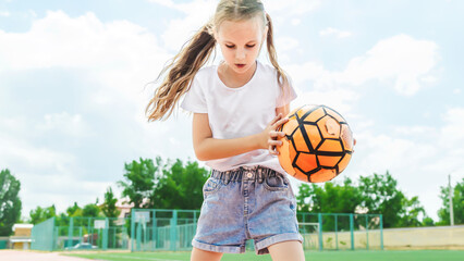 Caucasian preteen kid in casual outfit playing soccer ball outdoor in sunlight