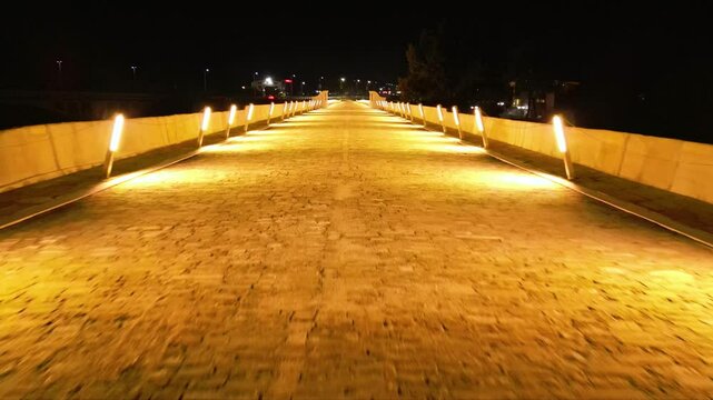Aerial high angle footage of a 150 years old stone masonry bridge illuminated on a dark night. Drone shot of the bridge at Byala village over the river of Yantra in Bulgaria.
