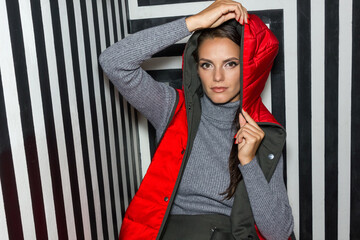 Young woman in red quilted down vest poses gracefully on creative striped background.