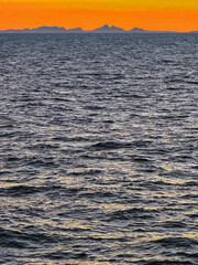 Obraz premium Seascape at sunset with a sihouette of the coast of Greenland on the horizon