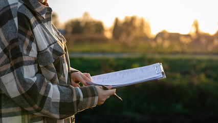 A Person Holding a Clipboard With Documents While Standing in a Field at Sunset, Reflecting on the Day's Work and Surroundings