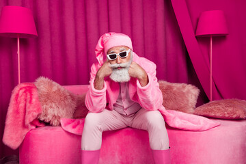 Photo of upset old man in bathrobe santa claus hat sitting couch feel bad indoors pink color barbie...