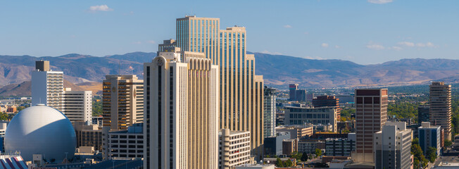 Reno, Nevada's skyline is seen from above, featuring the silver dome of the National Bowling Stadium and the Sierra Nevada mountains in the background. © Aerial Film Studio