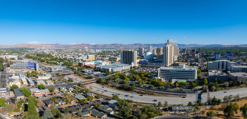 Naklejka premium Aerial view of Reno, Nevada, USA, featuring high rise buildings, casinos, and hotels. The Sierra Nevada mountains and Truckee River are visible under a clear sky.