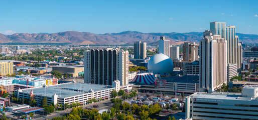 Aerial view of Reno, Nevada, showcasing the Silver Legacy Resort Casino's silver dome, modern high rises, and Sierra Nevada mountains in the background. © Aerial Film Studio