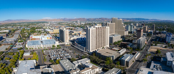 Daytime aerial view of Reno, Nevada, showcasing the Circus Circus hotel and casino, tall buildings, grid patterned streets, and distant mountains.