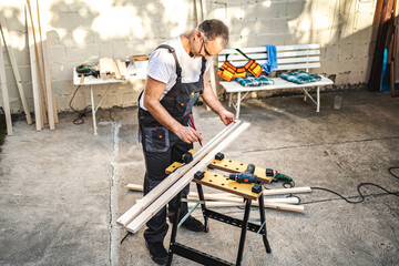 Mature male carpenter measuring wooden plank outdoors