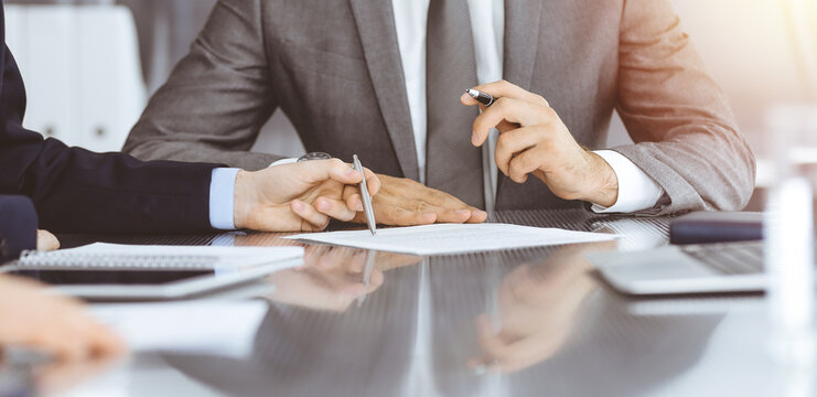 Unknown business people working together at meeting in modern office, close-up. Businessman and woman with colleagues or lawyers discussing contract at negotiation