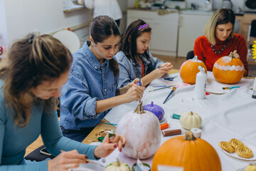 Fototapeta premium Children and adults painting pumpkins for Halloween, enjoying a fun and creative activity together.