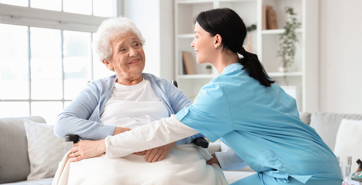Female nurse caring about senior woman in wheelchair at home