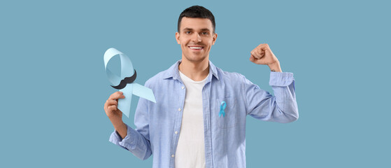 Young man with blue ribbon and paper mustache on color background. Prostate cancer awareness concept