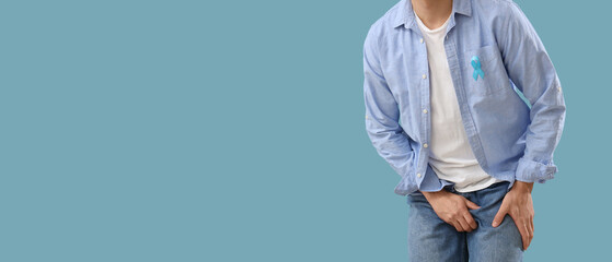 Young man with blue ribbon on color background, closeup. Prostate cancer awareness concept
