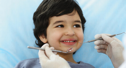 Cute arab boy sitting at dental chair with open mouth during oral checking up with doctor. Visiting dentist office. Stomatology concept