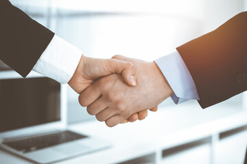 Businessman and woman shaking hands in sunny office, close-up. Concept of handshake as success symbol in business