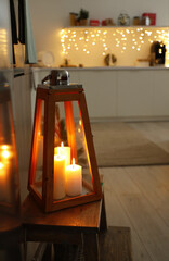 Lantern with burning candles on stool in kitchen decorated for Christmas