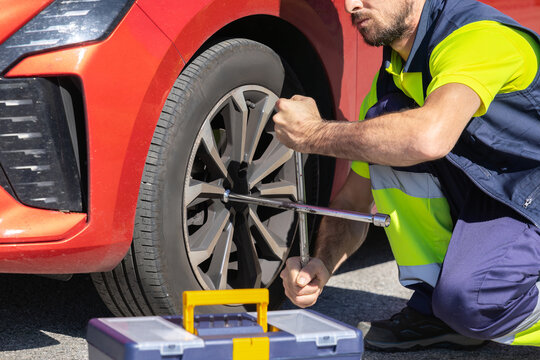 Young professional mechanic changing flat tire broken vehicle on the road with reflective clothing, toolbox and cross wrench, broken engine, roadside assistance, insurance tow truck - Powered by Adobe