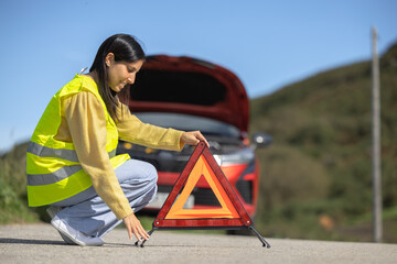 Pretty young woman poses in closeup placing emergency triangle sign and reflective vest on the...