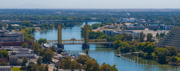 Aerial perspective of Sacramento, California, highlighting the yellow gold Tower Bridge over the Sacramento River, with urban and natural landscapes.