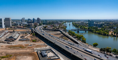 Aerial view of Sacramento, California, featuring a major highway, the Sacramento River with a bridge, and the iconic Ziggurat building under a clear sky.