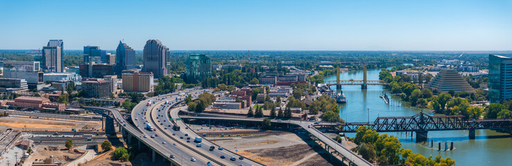 Obraz premium Aerial view of Sacramento, California, highlighting the golden Tower Bridge, the Ziggurat building, modern skyline, and lush greenery along the river.
