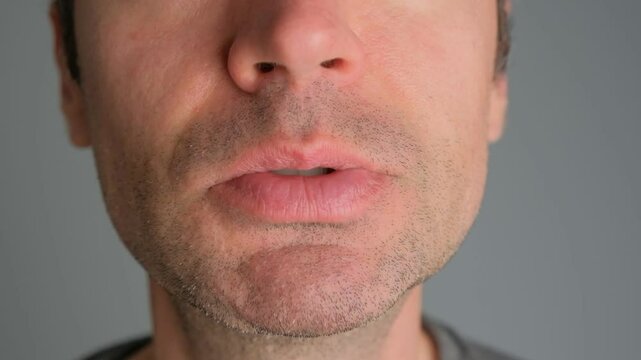 A man shows his tongue close-up on a gray background.
