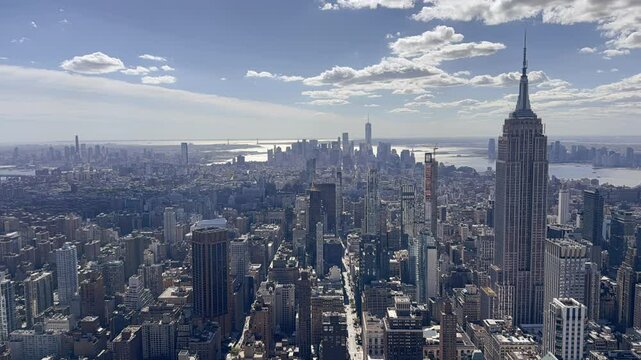 Stunning high angle time lapse footage capturing the iconic New York City skyline, featuring landmarks against a backdrop of clear blue skies and vibrant clouds. The view encompasses the vast urban la
