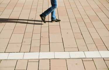 Blaue Jeanshosenbeine und braune Schuhe von über Platz gehender Mann mit Schattenreflexion in Stadt bei Sonne am Nachmittag im Herbst