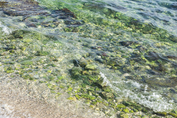 Rocky shore with waves crashing against stones. Transparent turquoise water. Beautiful beach backdrop for swimming and ocean vacations. Ocean vacations along the coast.