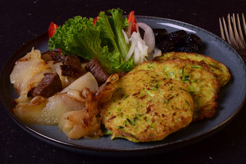 Vegetables and meat on a blue plate. Zucchini pancakes, beef, olives, potatoes