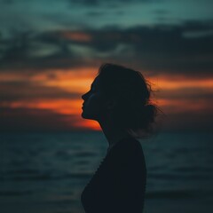 Fototapeta premium A woman’s silhouette is captured at sunset, overlooking the sea.
