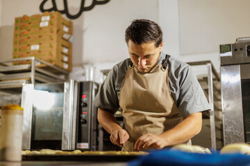 A Mexican baker in the bakery meticulously prepares pan dulce, demonstrating a high level of...