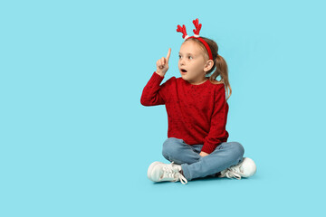 Emotional little girl in reindeer horns on blue background