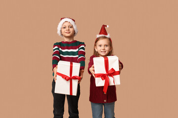 Cute little children in Santa hats with Christmas gifts on beige background
