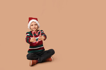 Cute little boy in Santa hat with candy canes on beige background