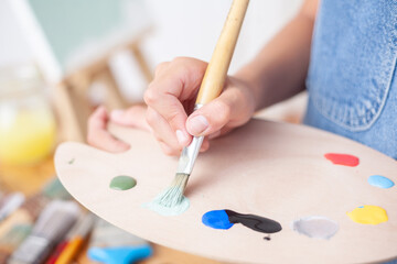 Naklejka premium Hands of a person painting a picture with a brush on a palette.
