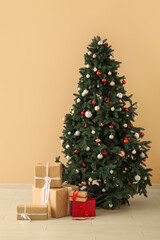 Beautiful Christmas tree with gift boxes near beige wall