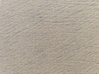 Natural patterns in the beach sand created by wind and waves, highlighted by soft, warm sunlight, form intricate lines and textures in a serene coastal setting.