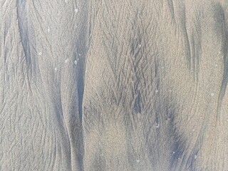 Natural patterns in the beach sand created by wind and waves, highlighted by soft, warm sunlight,...