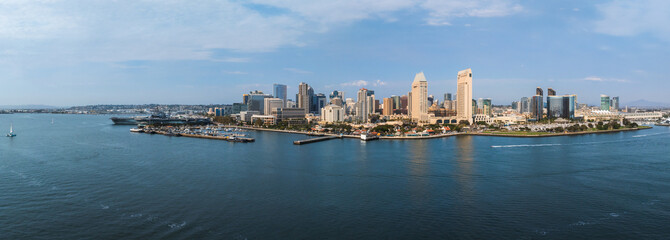 San Diego's skyline features skyscrapers like One America Plaza and Manchester Grand Hyatt. The San Diego Bay, with boats and the USS Midway, is visible.