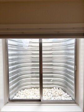 Clean Metal Window Well with White Decorative Stones Viewed from Basement Window