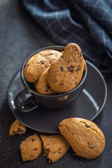 Biscotti frollini con gocce di cioccolato. Chocolate cookies in coffee cup on black table.
