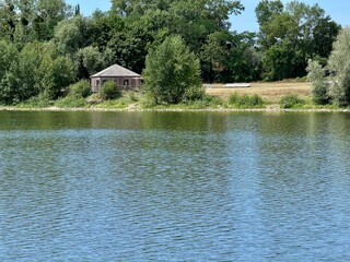 view of a small wooden cabin on the edge of a lake on a summer day with green vegetation
