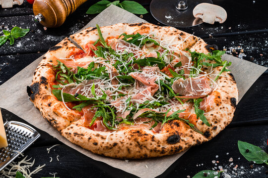 Pizza with slices of beef, arugula, parmesan cheese, tomato sauce and spices on thick dough from the oven.