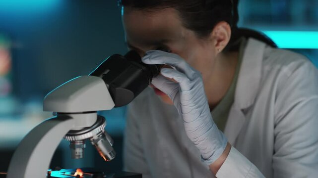 Asian female food scientist studying sample of cultured meat under microscope while conducting research in laboratory
