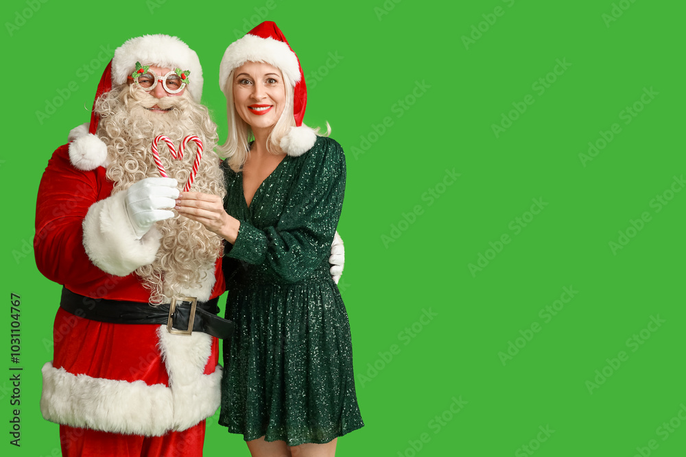 Wall mural Santa Claus and beautiful mature woman in Christmas hats with candy canes on green background