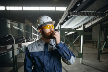 Worker of industry factory in uniform and hardhat use walkie-talkie for control conveyor on production