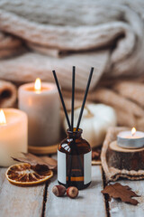 Home comfort, coziness, aromatherapy. Cozy interior with knitting, burning candles and aroma perfume diffuser in the living room. Fall scent, sweet pumpkin pie fragrance, dry leaves, autumn mood