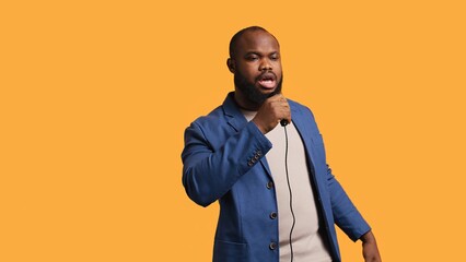 Smiling singer holding microphone, performing tunes during concert isolated over yellow studio background. Merry musician singing to imaginary crowd, performing on scene, camera B